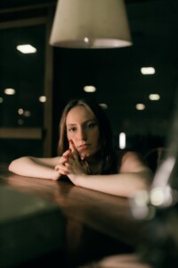 A contemplative woman in a dimly lit indoor setting creates a moody atmosphere.