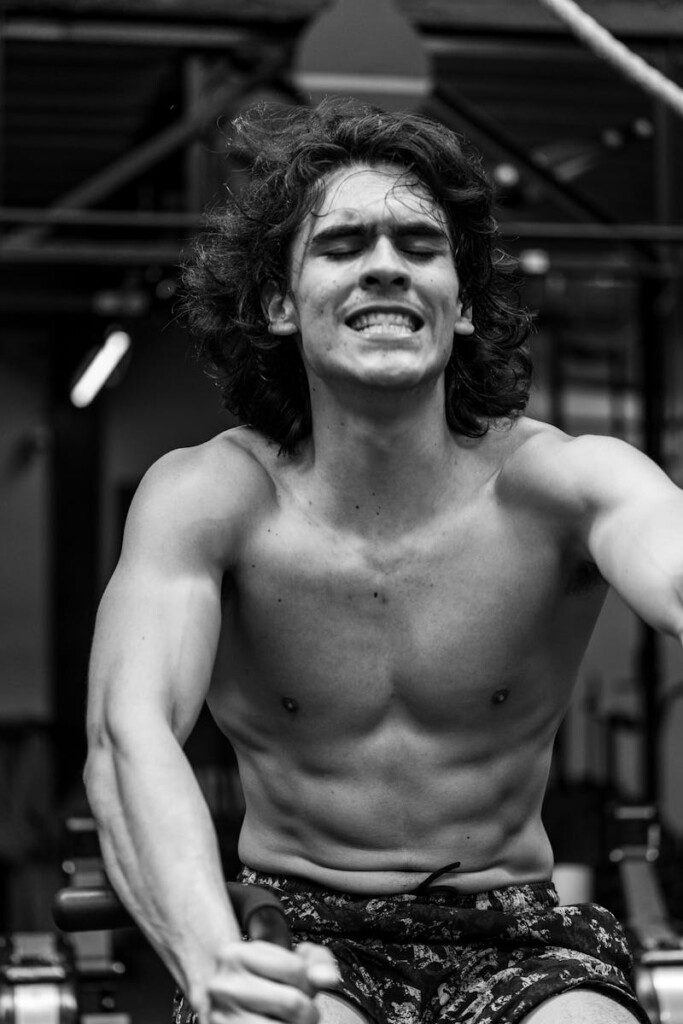 Determined young man intensely working out on a rowing machine in the gym.